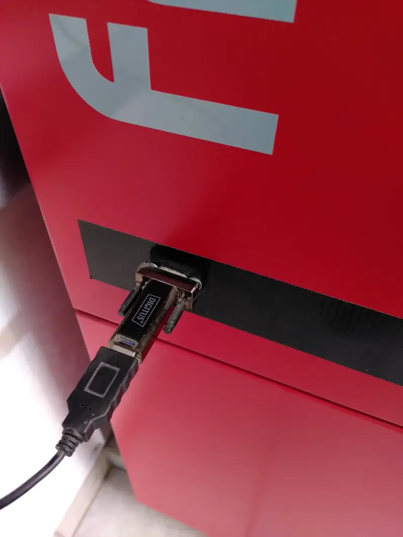 Nine-pin connector in the boiler's front cover with a USB-to-serial adapter and USB cable plugged in